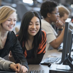 A multi-ethnic group of college age students are working together on a computer in the computer lab.