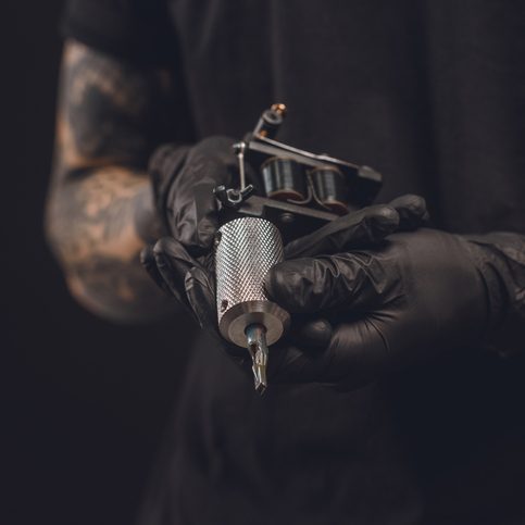 Joya tattoo Male hands in gloves holding tattoo machine isolated on black